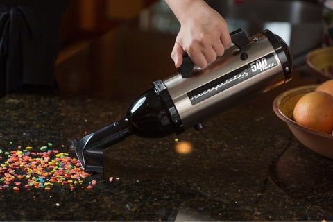 Evolution Hand Vacuum Portable 120V 504W With All Steel Construction For Dry Pickup At Home Office Or Car Satin Nickel Black Ultra Powerful Yet Lightweight For Quick Cleanups Everywhere, shown in use on a kitchen counter picking up cereal.