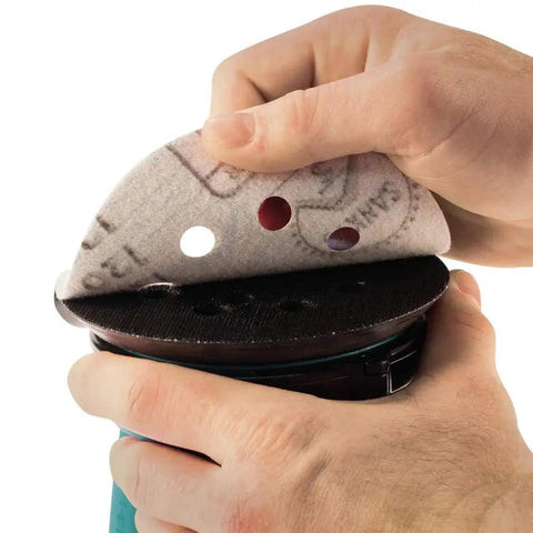 Hands attaching sandpaper to Cordless 5 Inch Random Orbit Sander 18V LXT With Three Speed Settings 7000 9500 11000 OPM