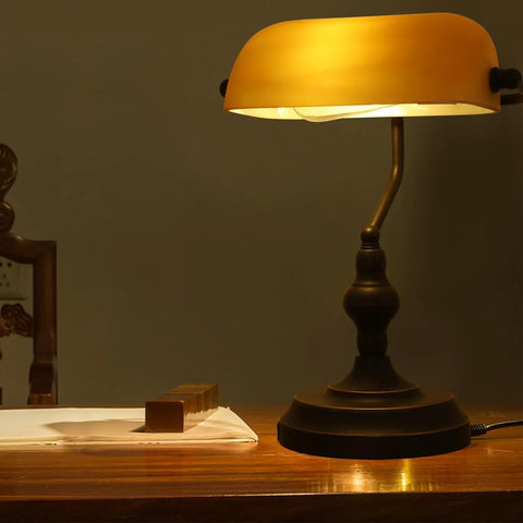 Jade Green Glass Vintage Banker Desk Lamp With Antique Brass Finish on wooden table in dim room, showcasing retro mid century vibe.