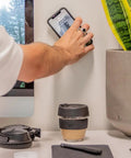 Person using Adhesive Phone Wall Mount Twin Pack For Non Porous Surfaces With 3M VHB Backing Sticks To Any Case Or Universal Adapters