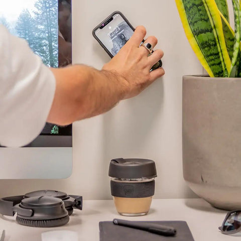Person using Adhesive Phone Wall Mount Twin Pack For Non Porous Surfaces With 3M VHB Backing Sticks To Any Case Or Universal Adapters