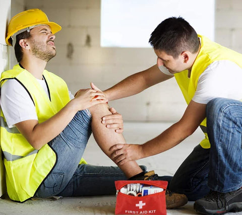 Red first aid kit bag with white cross, open to reveal medical supplies, on floor beside two workers in safety vests.