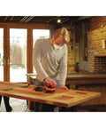 Person using Powerful Two Point Zero Amp Orbit Sander for finish work on a wooden table, demonstrating one-hand operation.