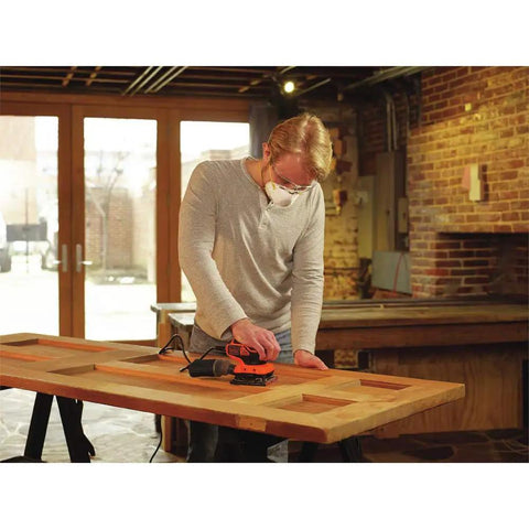 Person using Powerful Two Point Zero Amp Orbit Sander for finish work on a wooden table, demonstrating one-hand operation.