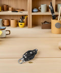 Black nylon pulley wheel single bearing block for marine & gym use on a wooden desk with stationery in background.
