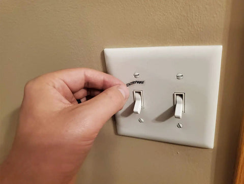 Person applying clear light switch labels transparent identifier system for home and office organization on a wall switch.