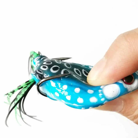 Close-up of 5 Pack Frog Lure Topwater Fishing Crankbaits Realistic Frog Soft Bait with 3D Eyes, blue pattern, held by hand.