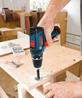 Person using 12V Max Drill Driver Kit With Two Batteries And Charger, Three-Eighths Inch Chuck, on wooden surface in workshop.