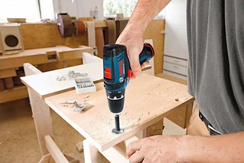 Person using 12V Max Drill Driver Kit With Two Batteries And Charger, Three-Eighths Inch Chuck, on wooden surface in workshop.
