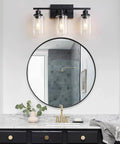 3 Light Black Vanity Light Fixture With Clear Glass Shades above round mirror in bathroom setting