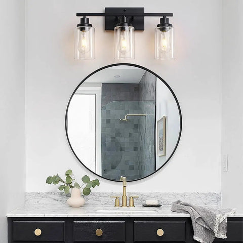 3 Light Black Vanity Light Fixture With Clear Glass Shades above round mirror in bathroom setting