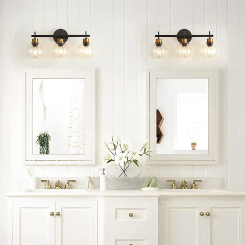 Three Light Black And Gold Bathroom Vanity Light Fixture With Metal Base And Clear Glass Globe Shades over two mirrors