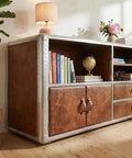 Knockout Aviator Sideboard Cabinet Drops That Aero Industrial Heat With Wraparound Weathered Brown Leather Riveted Silver Trim And Massive Storage Building A Solid 54 Inch Credenza Console Table For Any Cool Living Space with open shelves and drawers.