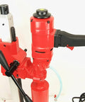 Red core drill with black grip handle mounted on a stand; power cord attached for concrete coring.