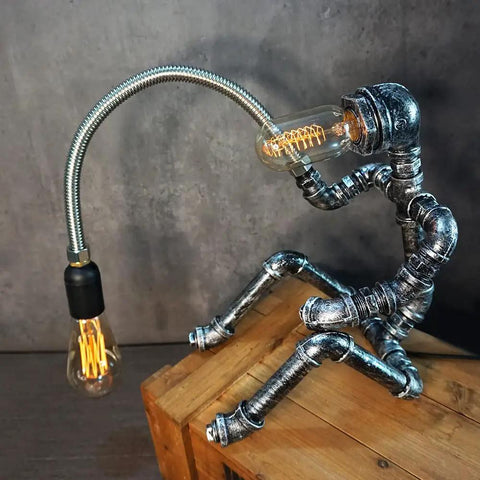Dope Handcrafted Steampunk Water Pipe Robot Desk Lamp With Vintage Industrial Vibe For Bedside And Desk, placed on a wooden box.
