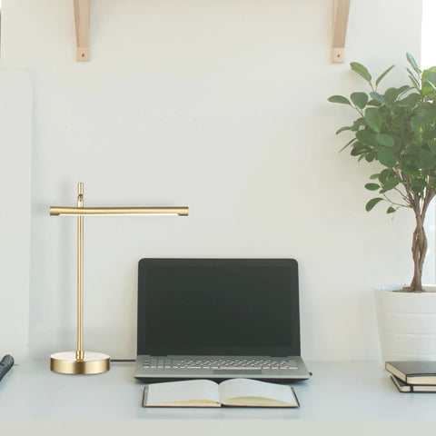 West 15 Inch LED Integrated Desk Lamp in matte brass on modern workspace with laptop and plant.