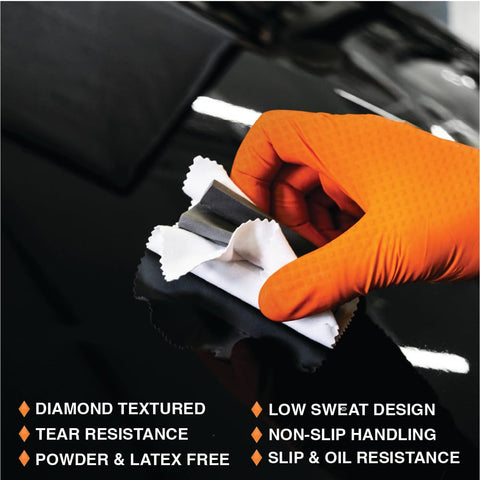 Person using Tough As Nails Eight Mil Orange Nitrile Work Gloves With Raised Diamond Texture for cleaning on a black surface.