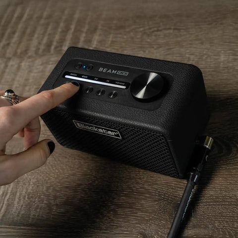 Person adjusting Beam Mini Portable Guitar Amp With NAM Compatibility, 17 Models, 35 Plus Effects, USB C And Bluetooth on wood surface.