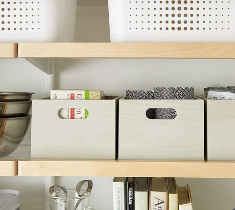 Wooden storage bins on a shelf with household items, showcasing organization in a modern kitchen or pantry.