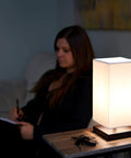 Lucerna 13-Inch Modern LED Touch Table Lamp With Oil Rubbed Bronze Finish and White Fabric Shade on nightstand next to person