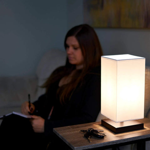 Lucerna 13-Inch Modern LED Touch Table Lamp With Oil Rubbed Bronze Finish and White Fabric Shade on nightstand next to person