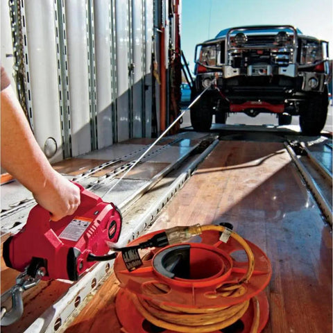 Heavy-Duty 120V AC Electric Winch With 1000 Lb Capacity For Vehicle Recovery, No-Load Line Speed Of 13.8 Fpm, Built Tough For Real-World Rugged Jobs, Easy To Use And Durable Winch That Replaces Outdated Come-Alongs. Handheld red 120V AC electric winch with wire rope pulling a vehicle onto a trailer.