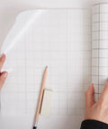 Frisket Masking Film Matte 10 Inch By 4 Yard Roll in use, artist applying film with pencil and eraser on grid surface