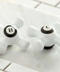 Close-up of porcelain cross handles for Heritage Widespread Lavatory Faucet With Porcelain Cross Handles In Oil Rubbed Bronze Solid Brass Construction Sleek 8 To 16 Inch Adjustable Center Deck Mount Three Hole Installation One Point Two GPM Flow IPS Connection Easy Install.