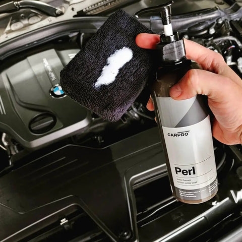 Hand holding Perl Coat Plastic And Rubber Protectant For Cars, Revives Dull Rubber, Plastics, Vinyl, Leather And Engine Bay Surfaces