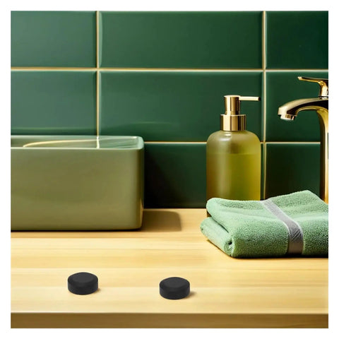 Bathroom sink with two black round objects resembling caps near faucet and towel, against green tiled wall.