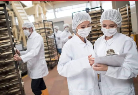 Workers in a food facility wearing Disposable Bouffant Hair Net Cap 21 Inch White Spun Bounded Polypropylene Head Cover 100 Count