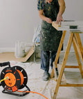Heavy Duty Retractable Sixty Foot Extension Cord Reel With Metal Stand next to a person working on a wooden sawhorse