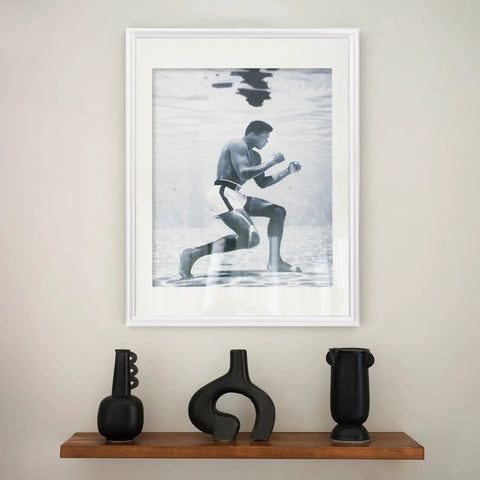 A framed photo of a person underwater above a shelf with modern black vases.