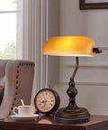 Jade Green Glass Vintage Banker Desk Lamp With Antique Brass Finish on a wooden side table next to a clock and cup in a cozy room.