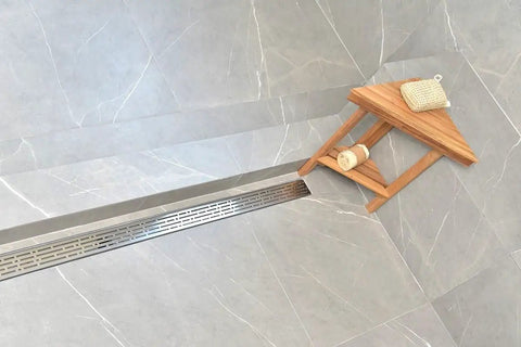 Top Shelf Heavy Duty SS304 Stainless Steel Linear Shower Drain With Integrated Hair Trap Anti Clog Catcher Rust Proof Corrosion Resistant Construction Perfect For Modern Bathroom Upgrades Sleek Design 59 Inch Span For Pro Results installed in modern bathroom with gray tiles and wooden stool.