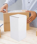 Person handling a shipping box with 10 Pack White Corrugated Cardboard Shipping Boxes With High Durability And Stable Weight Support nearby