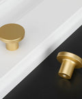 Gold cabinet knobs on white and black surfaces displaying a round design, not featuring Matte Black Cabinet Knobs 10 Pack.