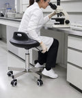 Heavy Duty Swivel Stool With Rock Solid Metal Build And Smooth Rolling Wheels For Studio Or Cleanroom Use Adaptable Design To Handle Your Daily Grind Without Breaking A Sweat in lab setting with user and microscope.