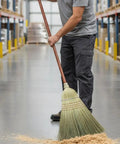 42 Inch Natural Fiber Wire Banded Warehouse Broom With Real Wood Handle For Sweeping Concrete Driveways Garages And Kitchens Built Tough To Handle The Daily Grind in use, sweeping sawdust in a warehouse aisle.