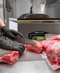 Heavy Hitter Chamber Vacuum Sealer With Rock Solid 1.5 Hp Rotary Oil Pump Built Tough For Commercial Chefs Keeps Food Fresh Five Times Longer Zero Downtime Design, chef slicing meat near sealing machine.