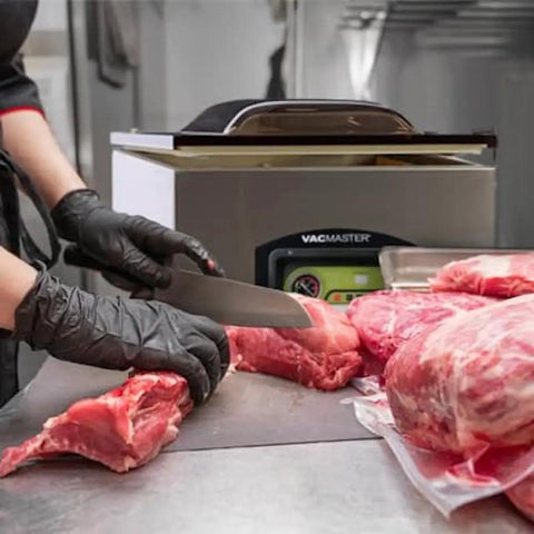 Heavy Hitter Chamber Vacuum Sealer With Rock Solid 1.5 Hp Rotary Oil Pump Built Tough For Commercial Chefs Keeps Food Fresh Five Times Longer Zero Downtime Design, chef slicing meat near sealing machine.