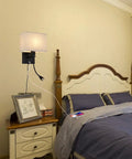 Plug In Black Wall Sconce With USB Port For Charging, Bedside Reading Lamp In Farmhouse Style next to a bed in a cozy bedroom