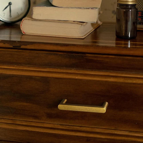 Set Of 6 Cabinet Pulls 3 Inch Center To Center Antique Brass Finish on wooden drawer with books on top