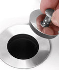 Person holding the Universals Bath Basins Waste Plug above a stainless steel sink hole, showcasing its rubber and stainless steel design.