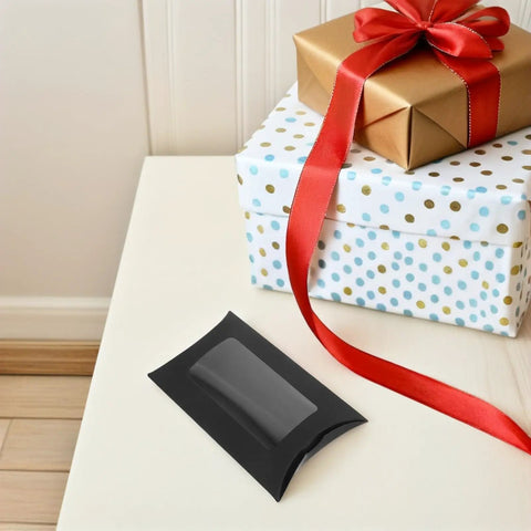 50 Pack Black Kraft Paper Pillow Gift Boxes With Window For Birthday Parties And Events displayed on a table with wrapped gifts.