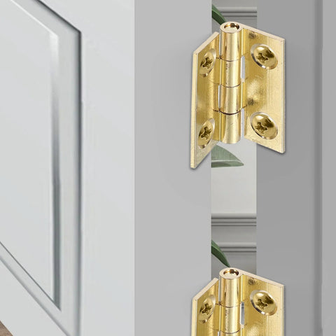 Two brass foldable cabinet door hinges with screws mounted on light gray cabinet doors
