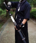 Person holding hand forged Longquan style dao sword with high carbon steel blade, full tang, matte black scabbard in outdoor setting.