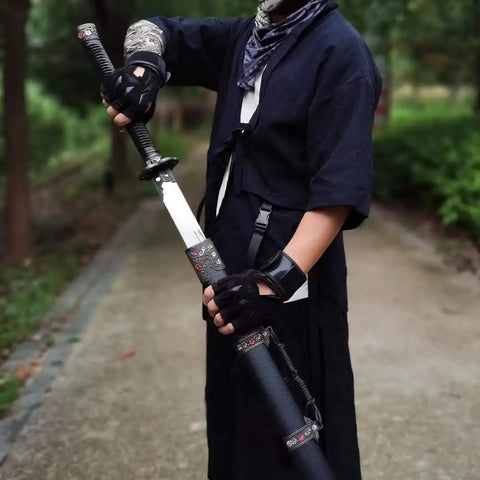 Person holding hand forged Longquan style dao sword with high carbon steel blade, full tang, matte black scabbard in outdoor setting.