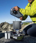 Hiker using 8 Piece Camping Cookware Mess Kit With Mini Backpacking Stove and Anodized Aluminum Nonstick Pots in mountain setting