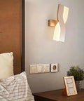 UPRENXIAO Modern Minimalist Nordic Led Wall Sconce Wavy Twisted Design Baked installed above a bed with soft light.